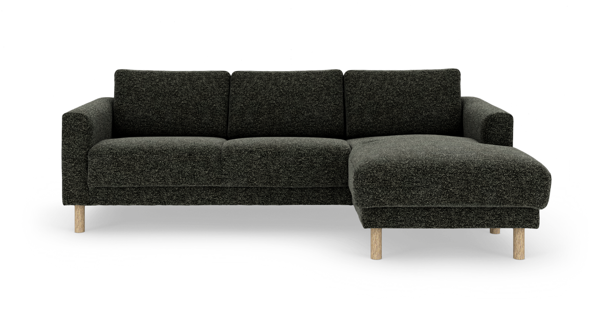 Mørkegrå stofsofa med højrevendt chaiselong og runde ben i lyst træ, fotograferet lige forfra på hvid baggrund.
