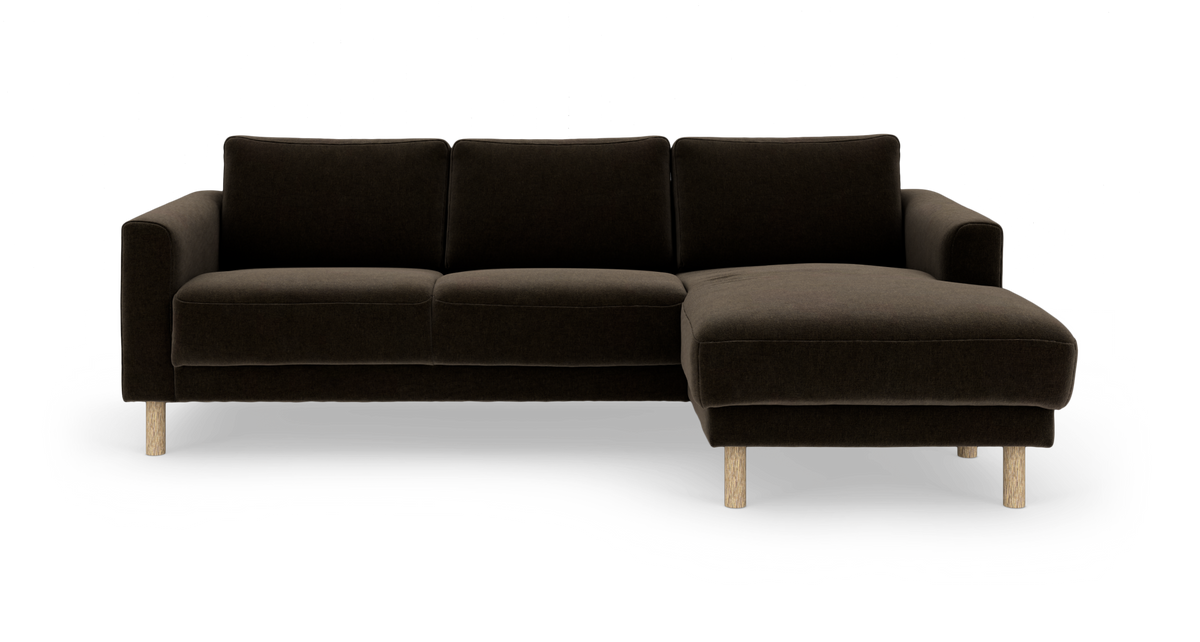 Mørkebrun hjørnesofa med chaiselong til højre og lyse træben, frilagt på hvid baggrund.