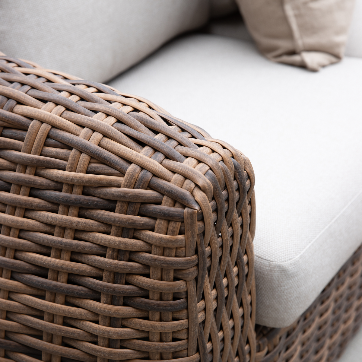 Nærbillede af flettet rattan-sofa med beige hynde og pude.