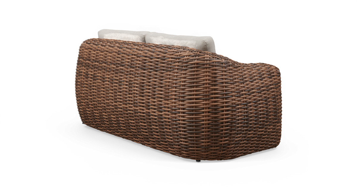 Bagside af brun fletsofa i rattan med lyse puder, fritlagt produktfoto.