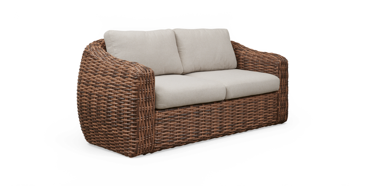 Tosædet flettet rattan-sofa med beige hynder, fritlagt i trekvart vinkel.
