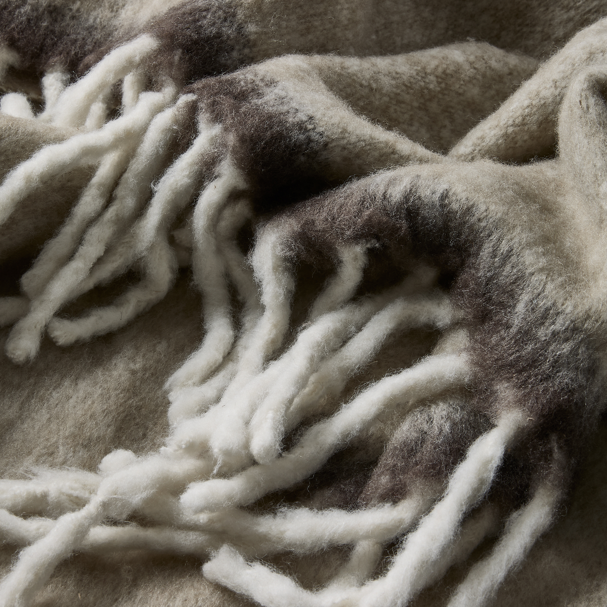Nærbillede af blød uldplaid med tykke frynser i beige og grå nuancer.