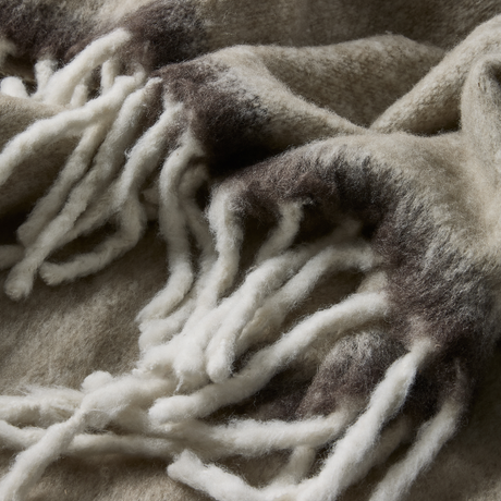 Nærbillede af blød uldplaid med tykke frynser i beige og grå nuancer.