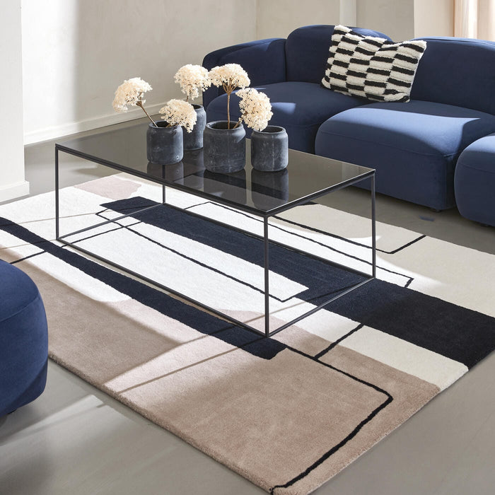 Moderne stue med mørkeblå sofa, sort glas-sofabord og grafisk tæppe i beige, sort og hvid samt vaser med tørrede blomster.