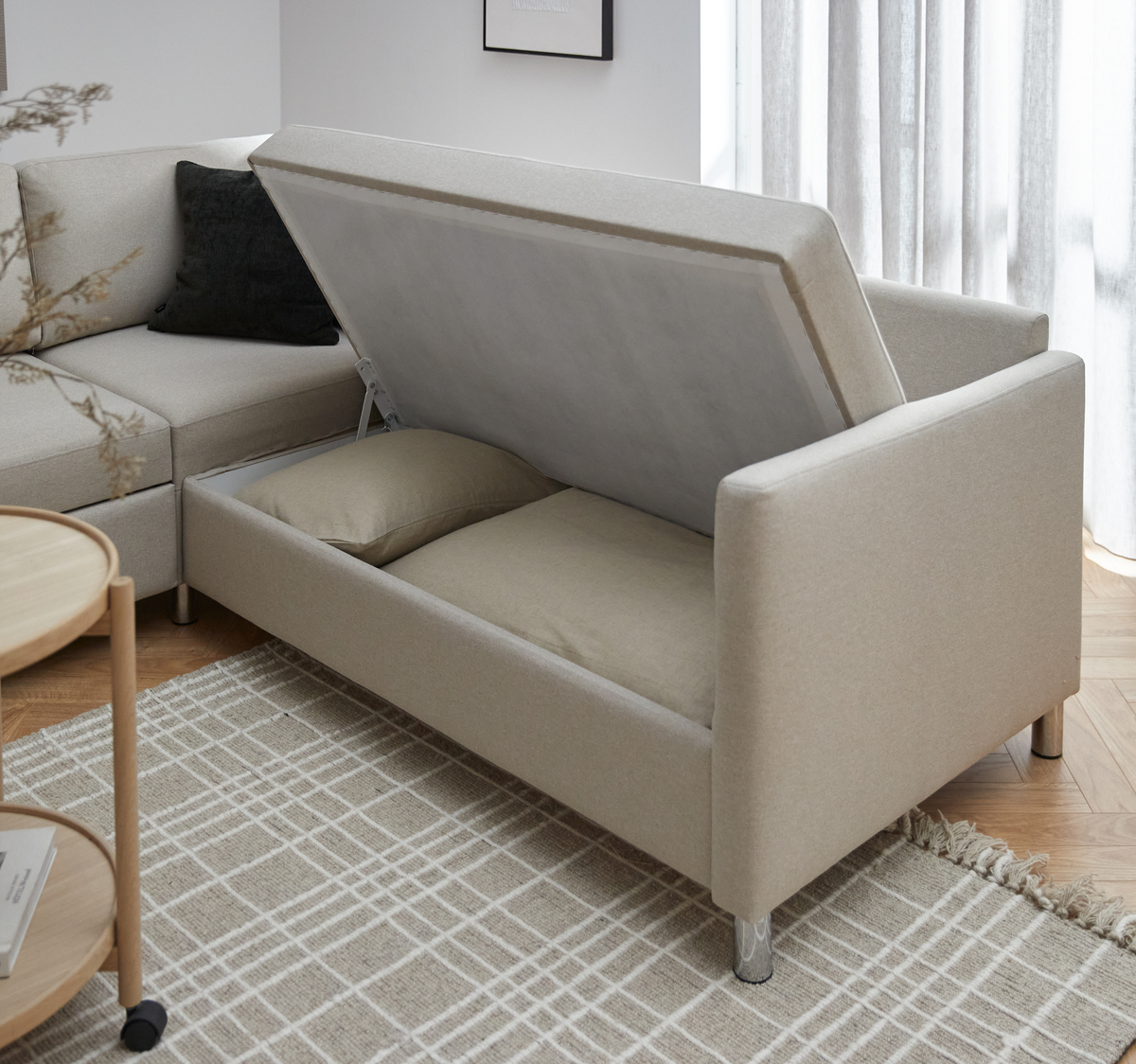 Beige sofa med opbevaring, sædet/låget løftet med puder indeni, i en lys skandinavisk stue.