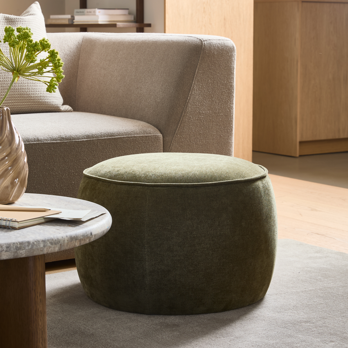Grøn rund puf foran beige sofa, marmorbord med vase og bøger i lys stue.