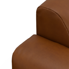 Nærbillede af et brunt læder-/læderlook sofa­hjørne med afrundet armlæn og sæde.