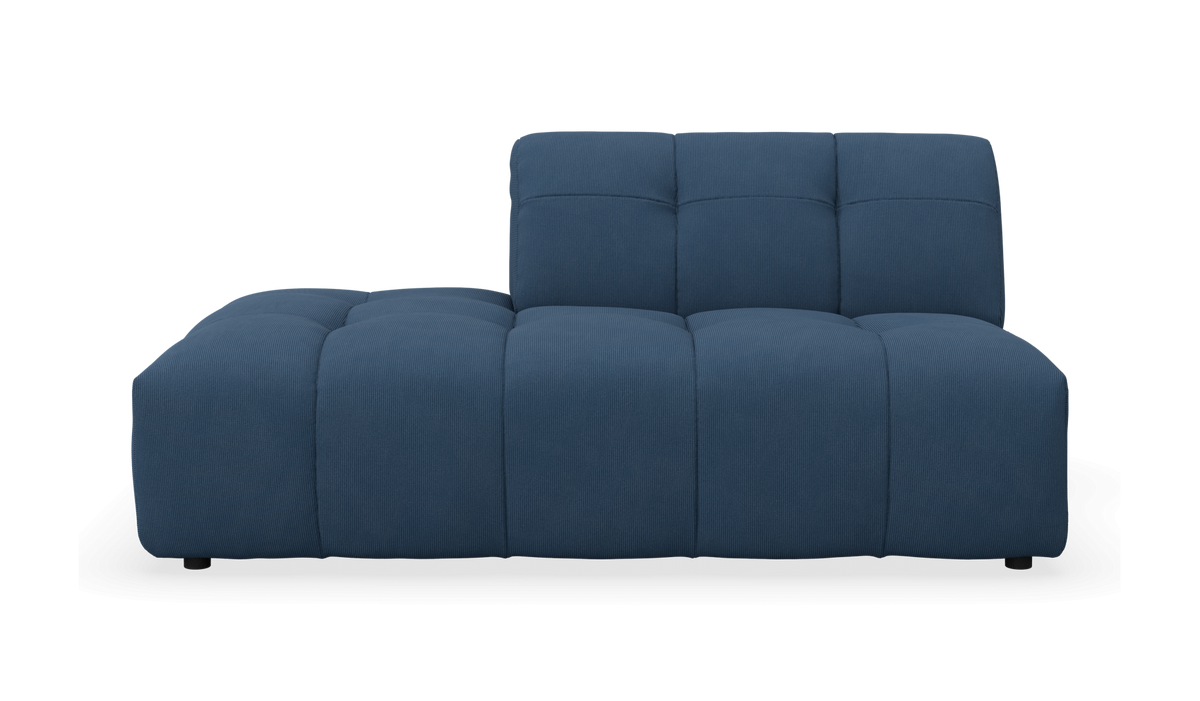 Frontview af en moderne blå modulsofa med lav venstre chaiselong og polstrede, søminddelte puder på hvid baggrund.