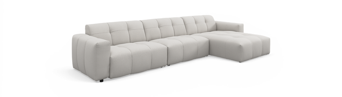 Lys beige modulsofa med højre chaiselong, lav og bred med blødt, quiltet stof og afrundede sektioner.