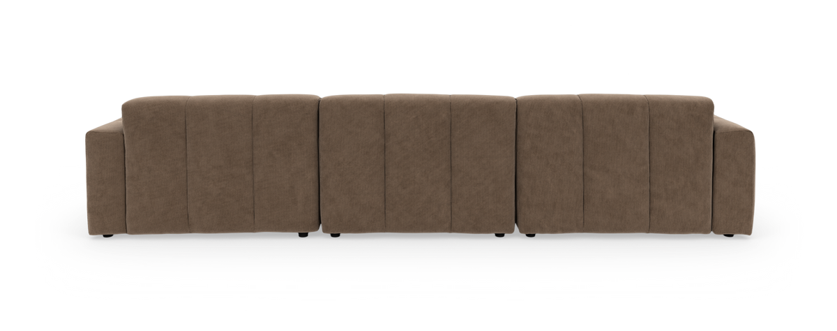 Beige modulsofa i fløjl med højrevendt chaiselong og tuftede, lave sædehynder, fotograferet forfra mod sort baggrund.