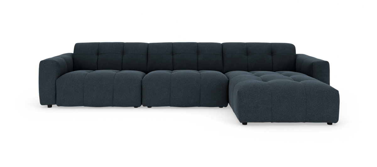 Mørkeblå modulsofa med højre chaiselong og tuftet polstring, fotograferet lige for i studie på hvid baggrund.