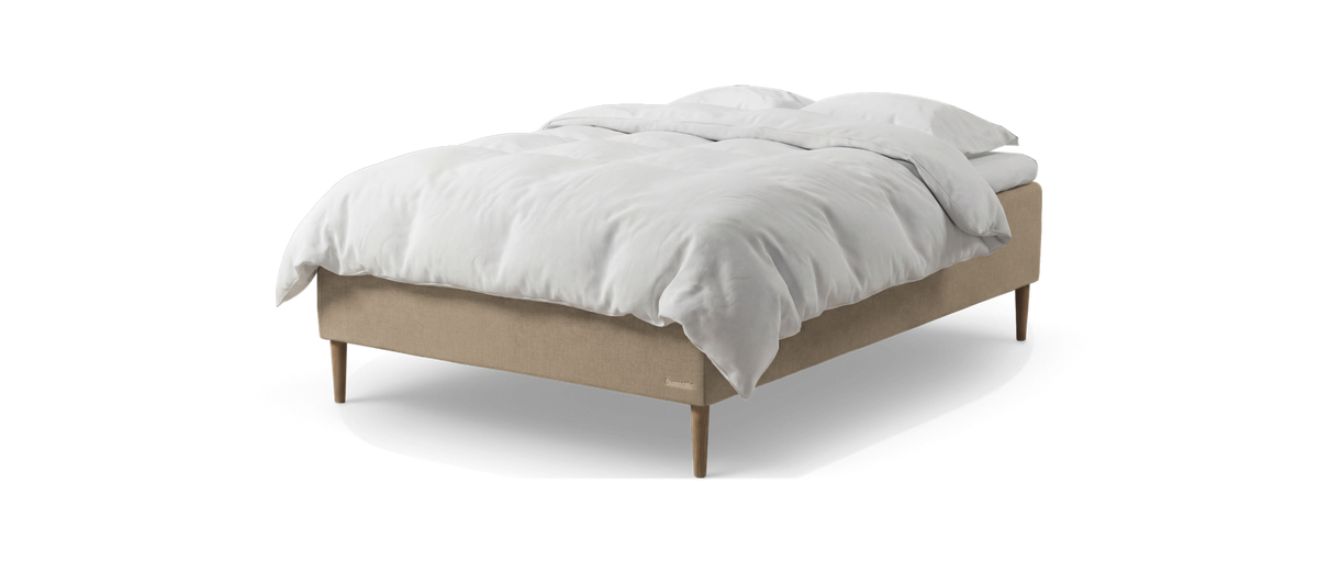 Beige seng med hvid dyne og puder, frilagt på hvid baggrund.