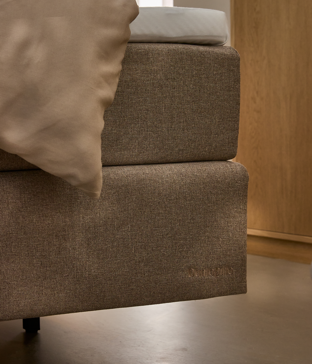 Nærbillede af beige sengebund med madras og pude; Dunlopillo logo i nederste hjørne.