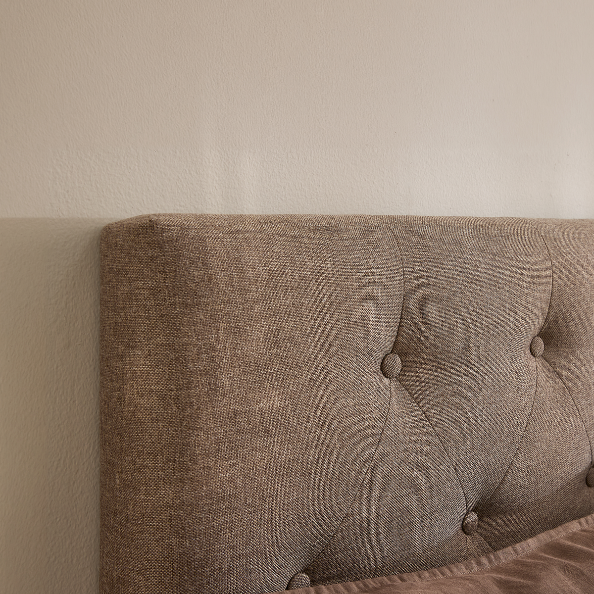 Beige knapstukket sengegavl i stof mod lys væg.