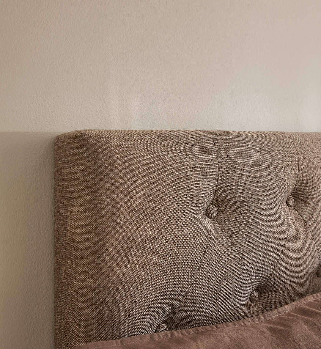 Beige, knap-tuftet polstret sengegavl mod en lys væg i et minimalistisk soveværelse.