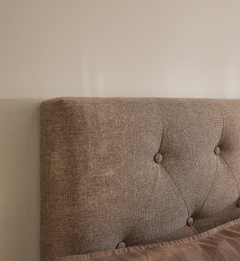 Beige, knap-tuftet polstret sengegavl mod en lys væg i et minimalistisk soveværelse.