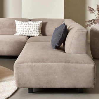 Beige hjørnesofa i stof med to pyntepuder, rundt lyst tæppe, sofabord i træ, pendellampe og stor vase med tørrede grene i en lys stue.