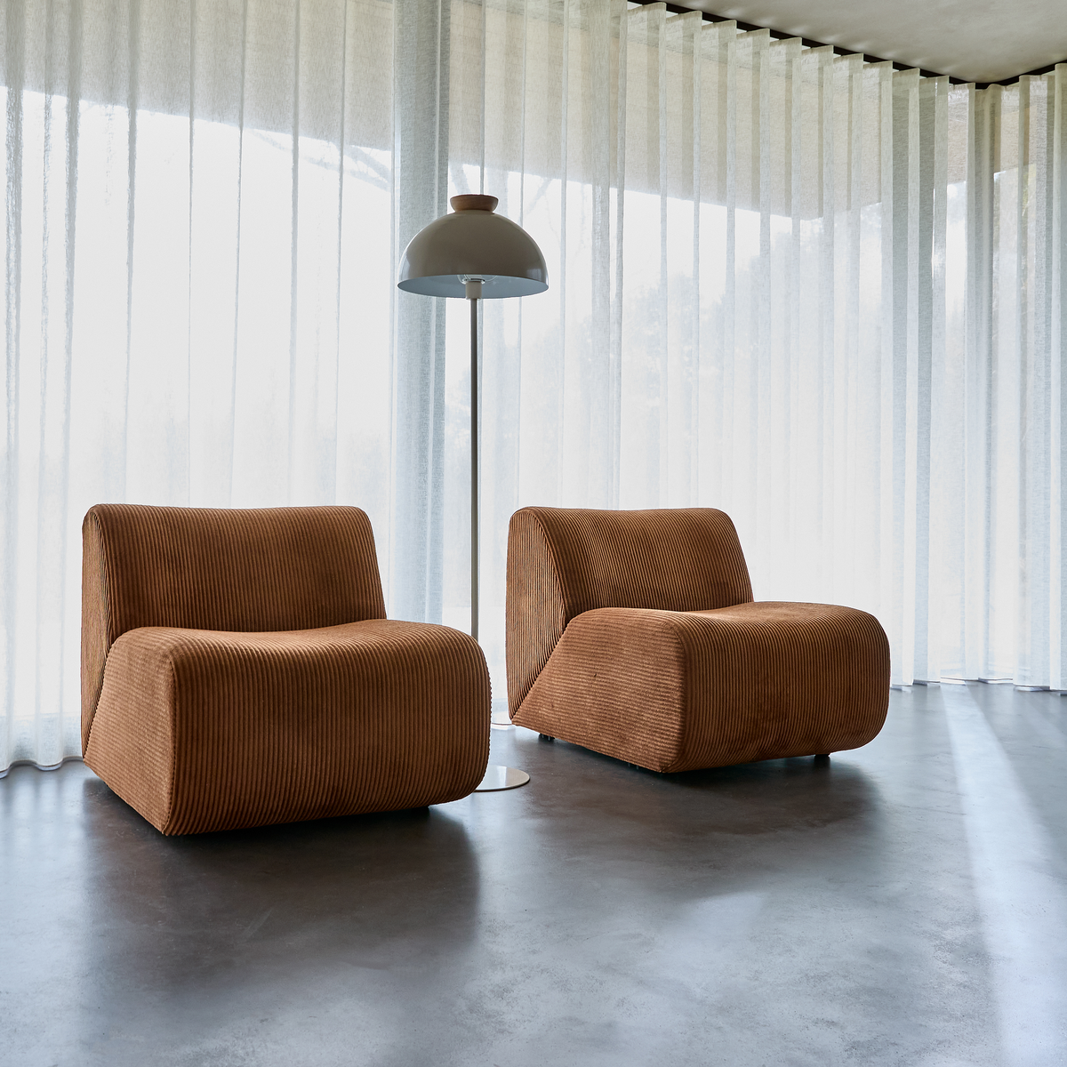 To brune loungestole i fløjl med standerlampe foran lyse, transparente gardiner.