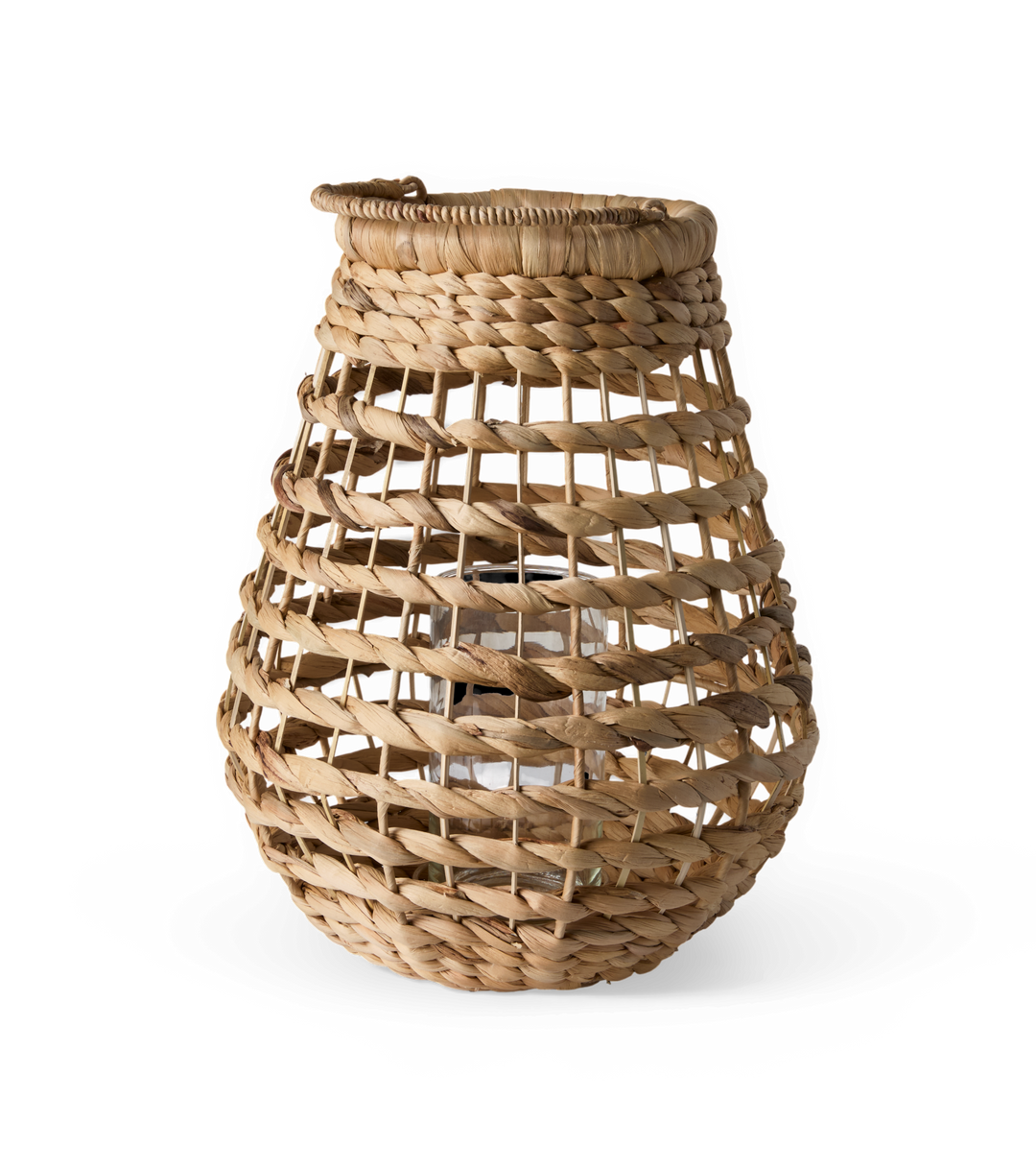 Flettet lanterne i naturfarvet rattan med glasindsats til lys, frilagt på hvid baggrund.
