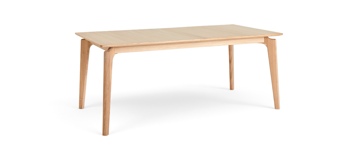 Rektangulært spisebord i lys eg med slanke, tilspidsede ben, fotograferet i vinkel mod hvid baggrund.
