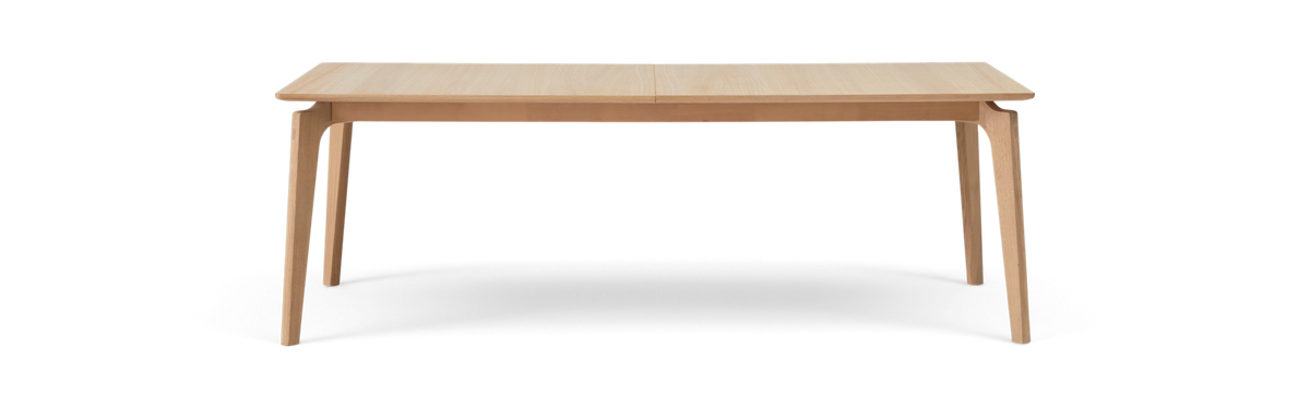 Rektangulært spisebord i lys eg med slanke skrå ben, fritlagt på hvid baggrund.
