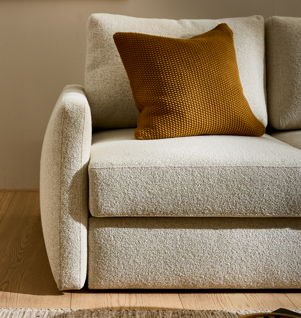 Beige bouclé-sofa med sennepsgul strikket pude i et solrigt hjørne af stuen.