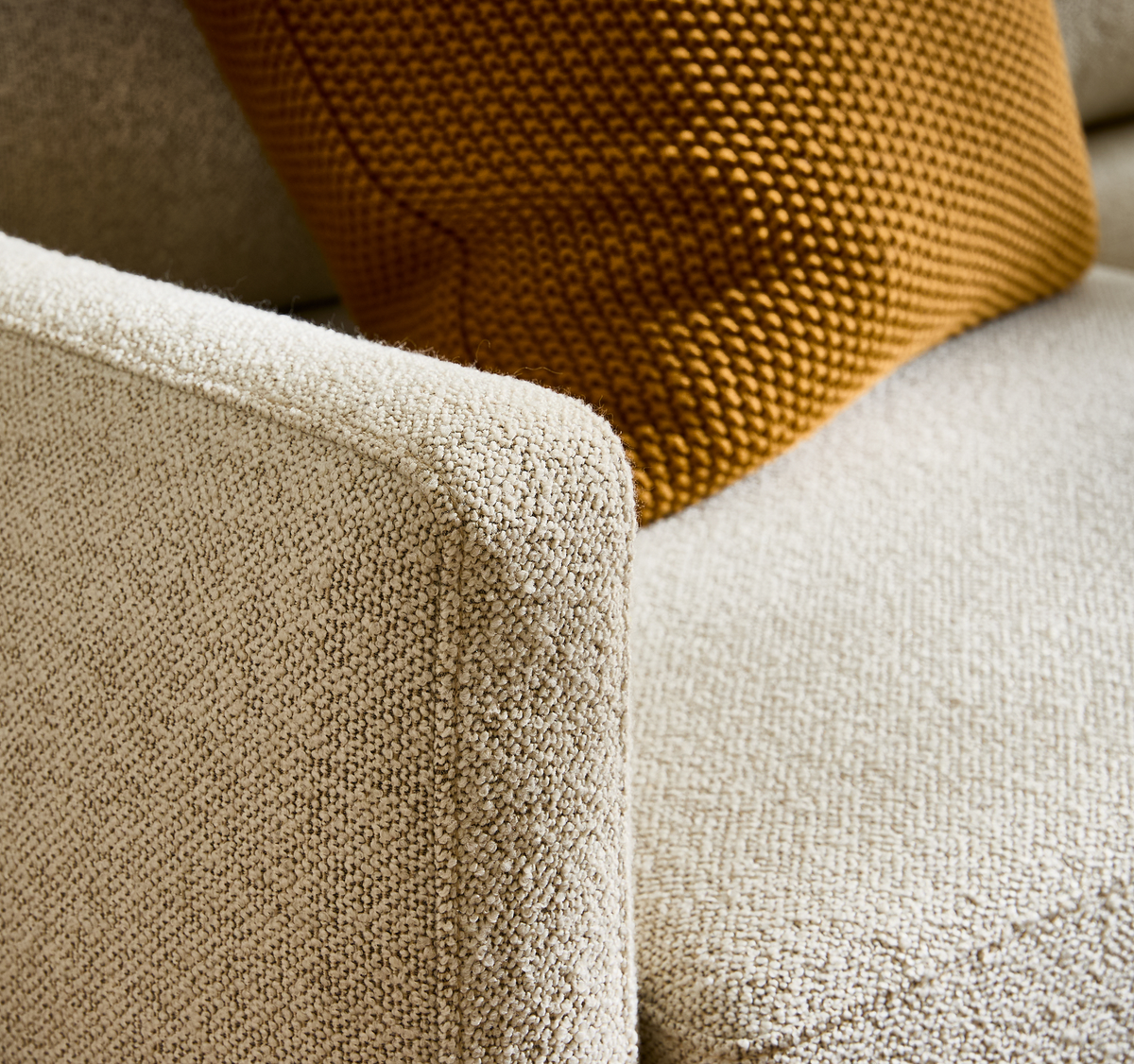 Nærbillede af beige bouclésofa med sennepsgul strikket pude.