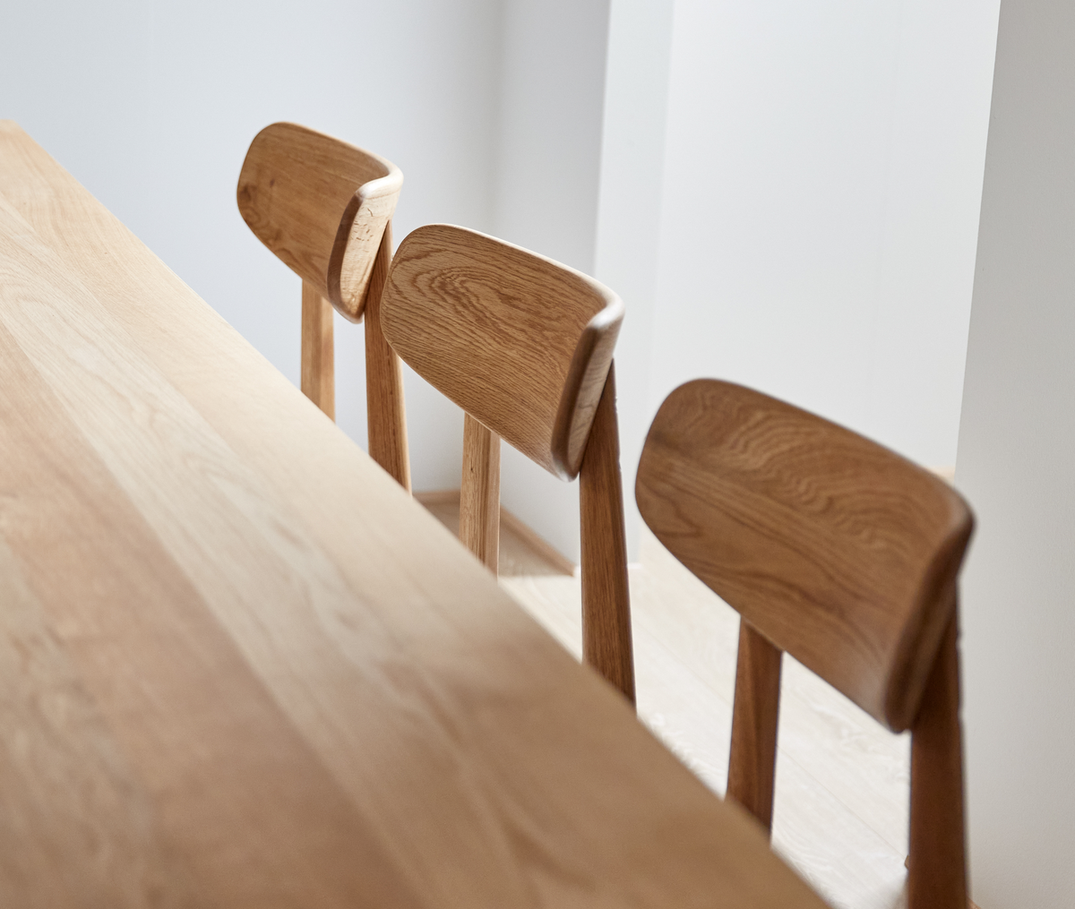 Tre spisebordsstole i lys eg ved et træbord i et lyst, minimalistisk rum.