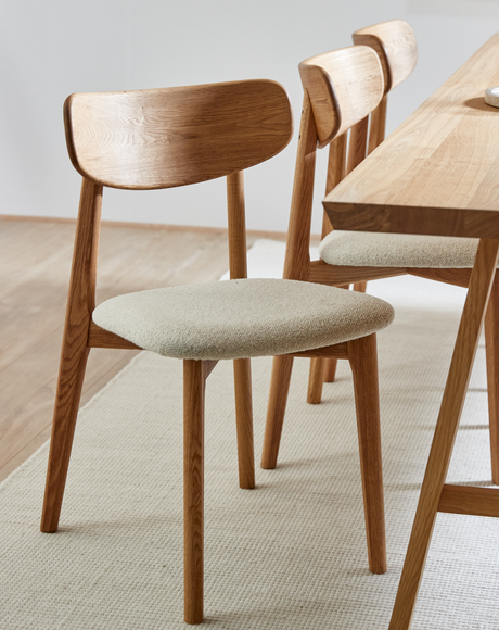 Egestole med lys polstret sæde ved siden af et matchende træbord på et lyst tæppe i et lyst, minimalistisk spisemiljø.