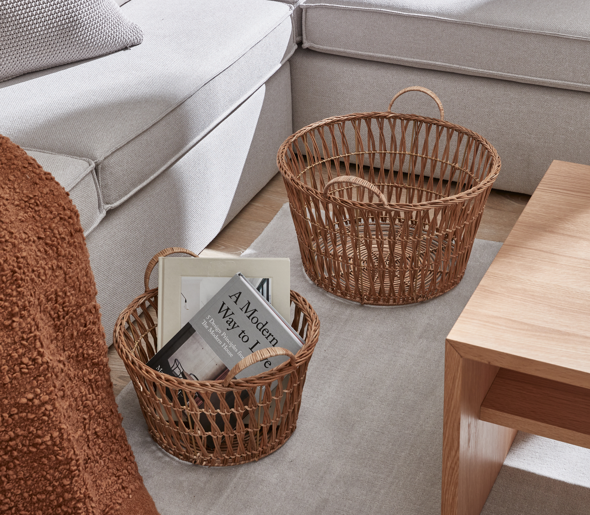 To flettede kurve ved siden af en lys sofa og sofabord; den mindre kurv rummer bøger, heriblandt A Modern Way to Live.