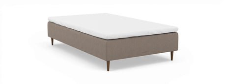 Beige sengebund med hvid topmadras og koniske træben, nocturne, frilagt på neutral baggrund.