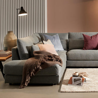 Grå modulsofa med puder i douce farver, væglampe over abstrakt kunst, gulvlampe, beige tæppe og strikket plaid i en varm stue.