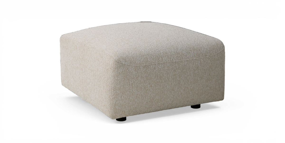 Beige kvadratisk stofpuf/ottoman med afrundede hjørner, set i skrå frontvinkel.