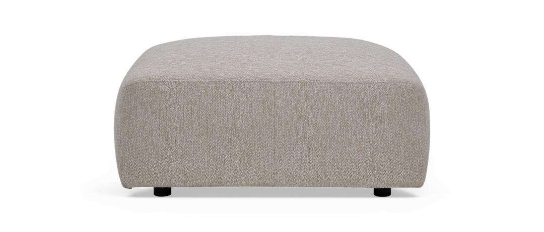 Beige firkantet puf/ottoman i stof med afrundede hjørner, set forfra.