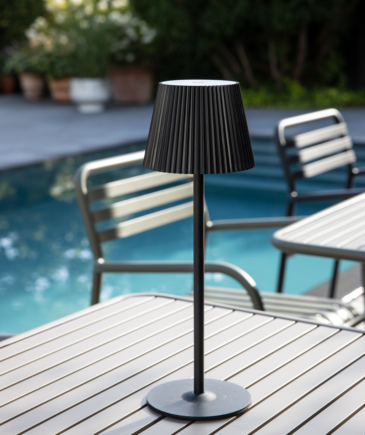 Sort bordlampe med rillet skærm på et lamelbord udendørs ved en pool.