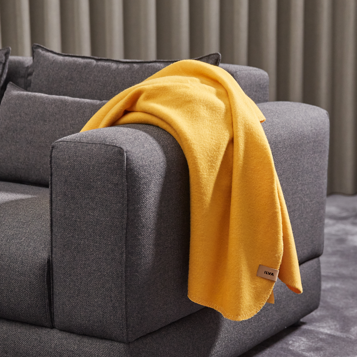 Grå sofa med gul plaid over armlænet, ILVA på mærket.
