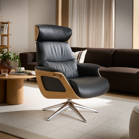 Sort læderlænestol med trædetaljer og blank drejefod i en lys skandinavisk stue med beige tæppe, brun sofa og sofabord med vase, bøger og grøn plante.