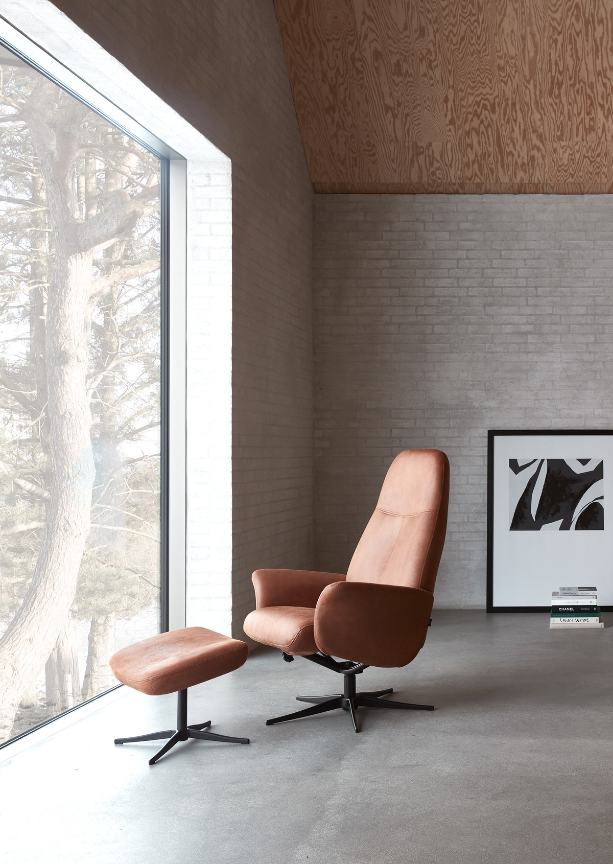 Lys, minimalistisk indretning med cognacfarvet drejestol og skammel ved et stort vindue, lys murstensvæg, abstrakt kunst og en bogstak med CHANEL i rolig skandinavisk stil.