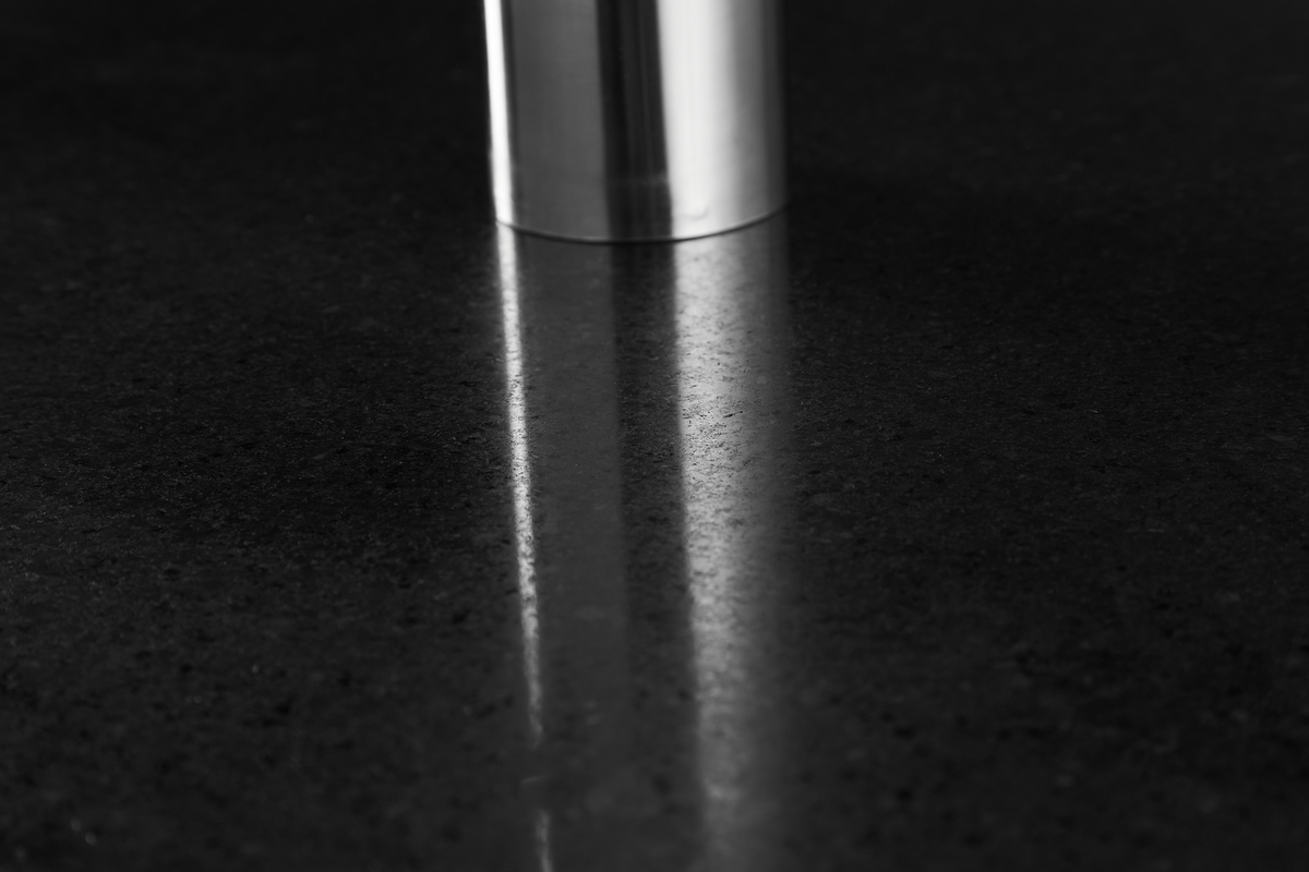 Blankpoleret mørk stenbordplade med spejling af en rustfri cylinder.