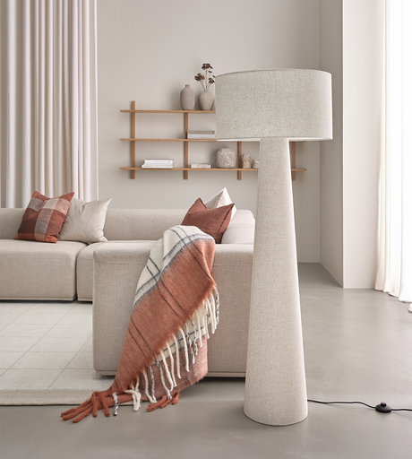 Lyst stue med beige sofa, terrakotta-puder og plaid, stor tekstil gulvlampe og træhylde med vaser i blødt dagslys.