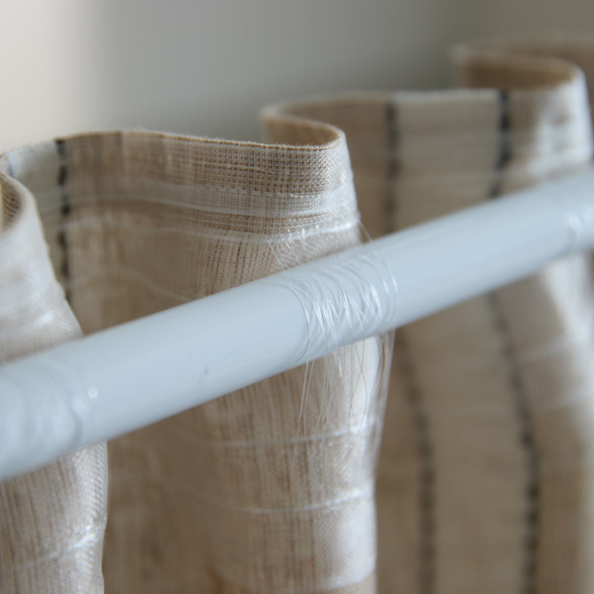 Nærbillede af beige, tekstureret gardinstof på en hvid gardinstang.