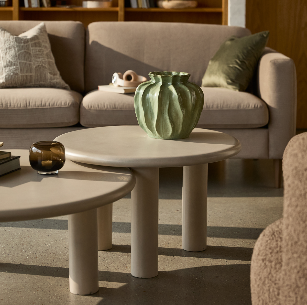 Beige runde sofaborde med skulpturel grøn vase i en varm, skandinavisk stue.