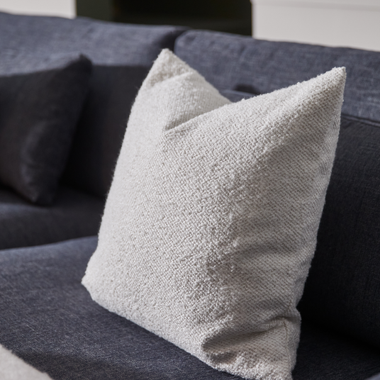 Nærbillede af en hvid, tekstureret pude på en mørkegrå sofa.
