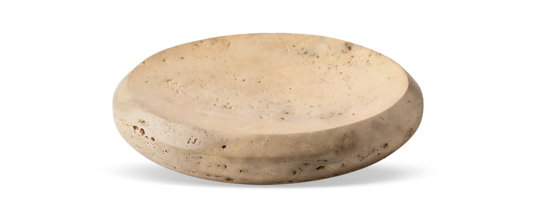 Beige rundt fad/skål i travertin med lav profil på sort baggrund.