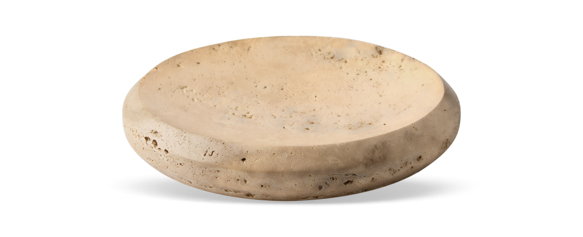 Beige rundt fad/skål i travertin med lav profil på sort baggrund.