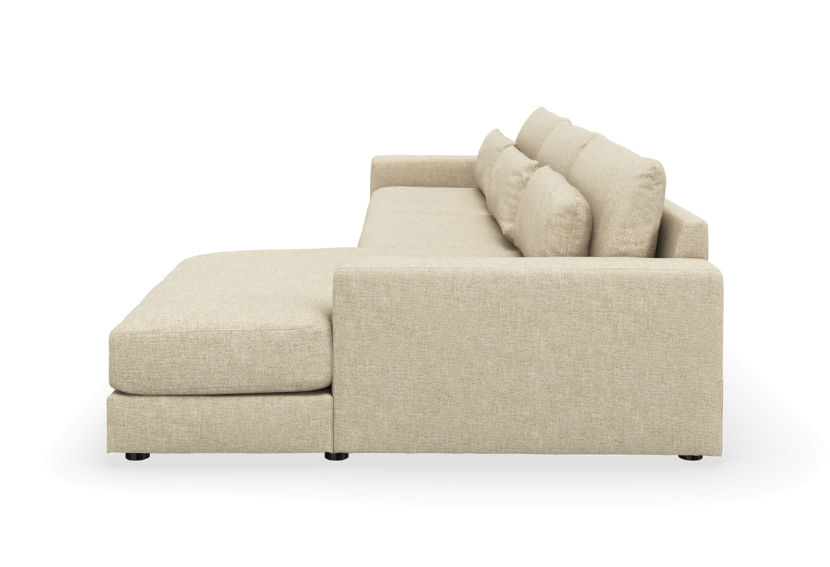 Beige L-formet hjørnesofa med venstrevendt chaiselong og bløde ryghynder, set fra siden på hvid baggrund.