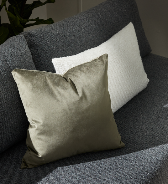 Nærbillede af olivengrøn velourpude på mørkegrå sofa med hvid tekstureret pude bagved.