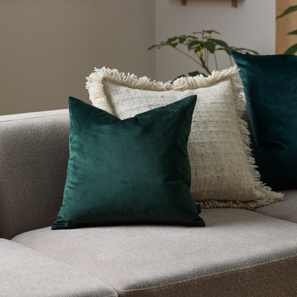 Mørkegrøn velourpude og beige frynset pude på beige sofa i stue.