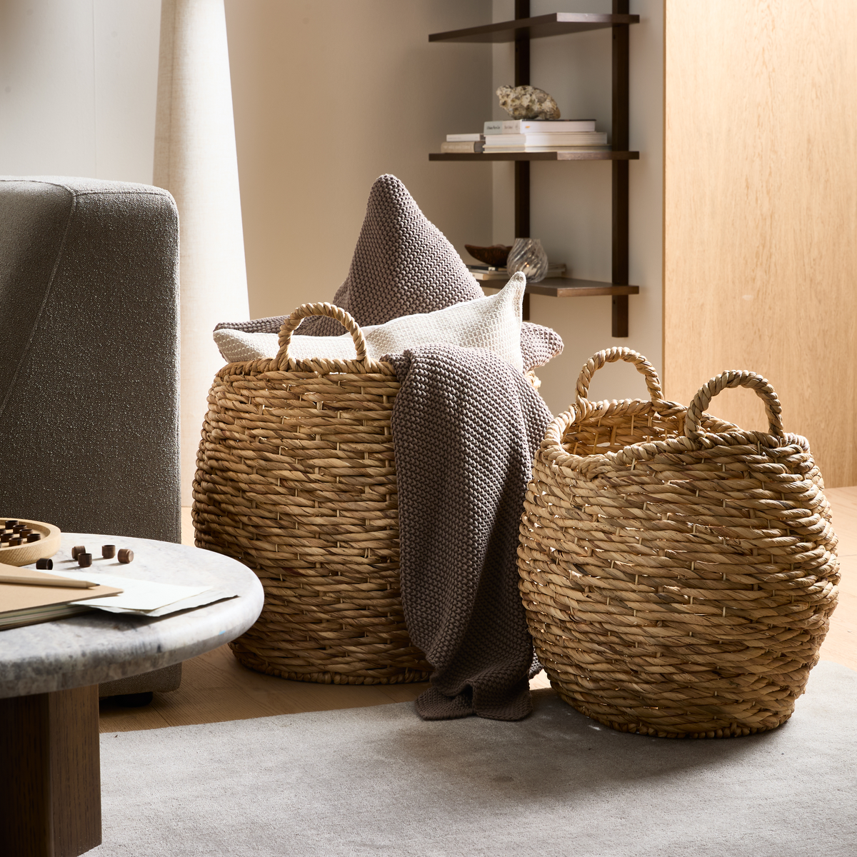 To flettede kurve i naturmateriale med plaid og puder i en lys stue.