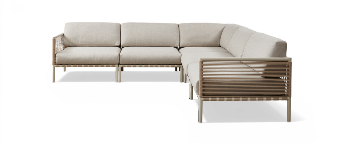Beige modulsofa i L‑form med flettede sider og slanke ben, frilagt på hvid baggrund.